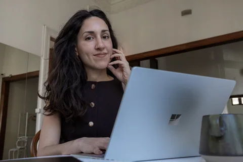 Una mujer mira hacia la cámara junto a una computadora portátil