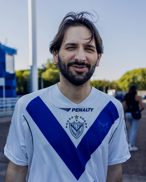 Retrato al aire libre de un hombre con camiseta de Vélez y un ojo entrecerrado