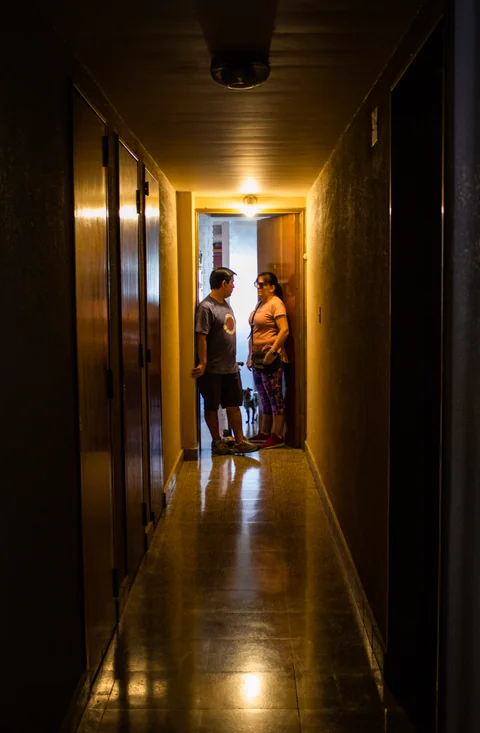 Dos personas conversan al fondo de un pasillo iluminado con luz cálida