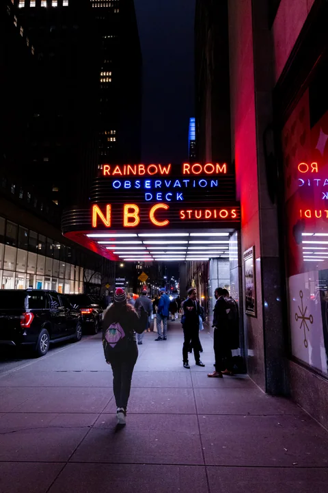 Una persona camina bajo los carteles luminosos de Rainbow Room y NBC Studios